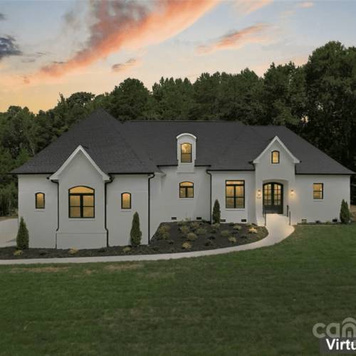New Project - 2024-12-26T125447.657 A large, two-story house with a white exterior and dark roof sits on a lawn, surrounded by trees, under a colorful sky at sunset.